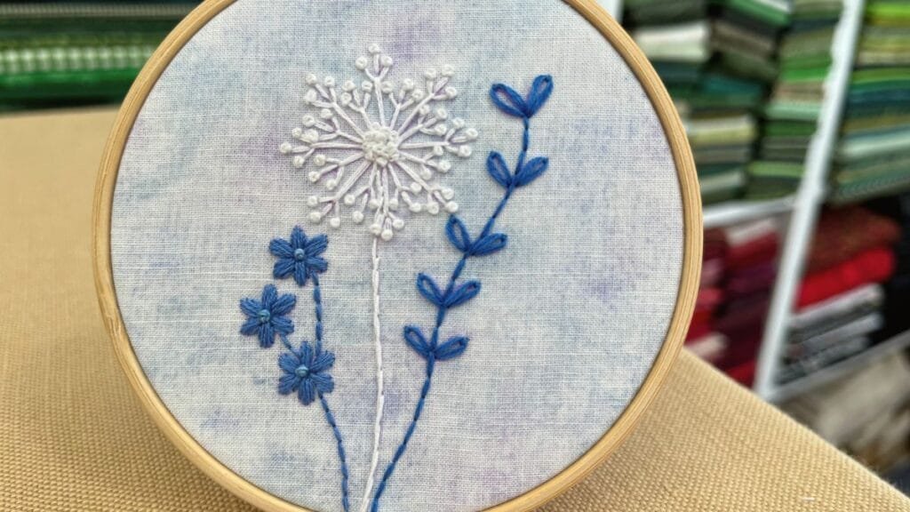 Photo of finished blue and white hand embroidery flowers in a hoop.